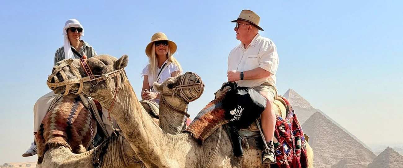 Trois voyageurs à dos de chameau devant les pyramides de Guizeh