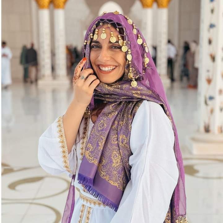 Voyageuse au foulard violet et pièces dorées souriant dans la salle de marbre blanc d'une grande mosquée